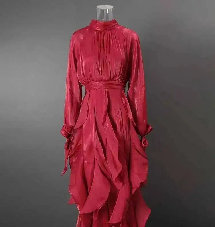 A vibrant red long-sleeve midi dress with a high gathered neckline, self-tie waist belt, and dramatic layered ruffle skirt, displayed on a mannequin against a dark gray background.